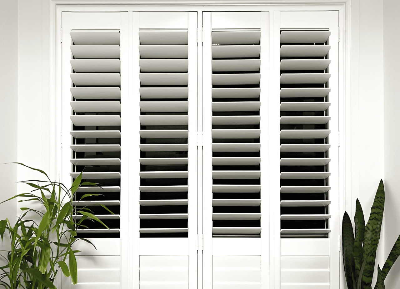 A white window with closed shutters, adorned with a green plant on the sill, creating a fresh and inviting atmosphere.